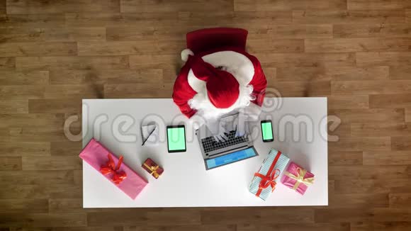 圣诞老人在办公室工作手提电脑智能手机和平板电脑带有色度绿色屏幕打字鸟瞰顶部视频的预览图