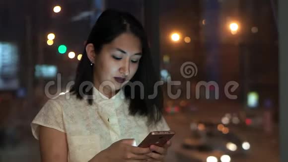 这个女孩在智能手机上阅读信息在办公室里带着大窗户对着夜城视频的预览图