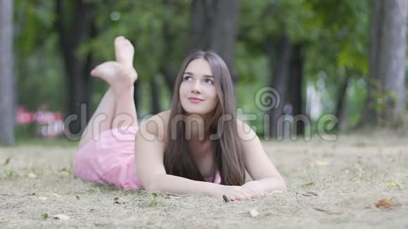 可爱迷人的女人躺在草地上微笑放松的女孩在公园里缓慢地做梦视频的预览图