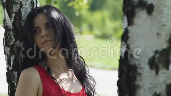 寂寞可爱的女人伤心地站在树下的公园里分手的关系视频的预览图
