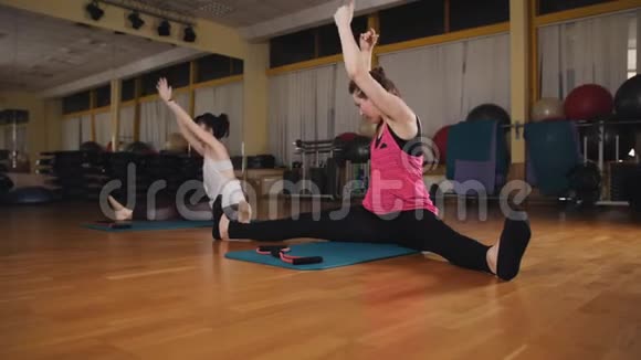 两个女孩做伸展运动女孩坐在地板上劈叉双手伸到脚边视频的预览图