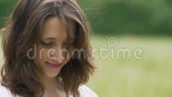 害羞美丽的年轻女人棕色头发微笑着看着户外的自然视频的预览图