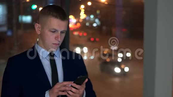 一个男人是个商人在他的智能手机上检查他的邮件靠近窗户和夜城视频的预览图