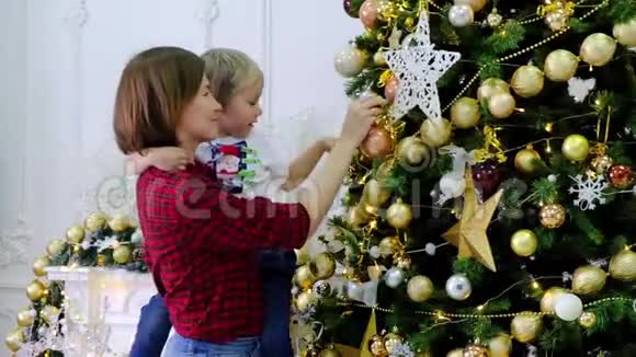 女人和她的儿子在房间里用金色玩具装饰圣诞树视频的预览图