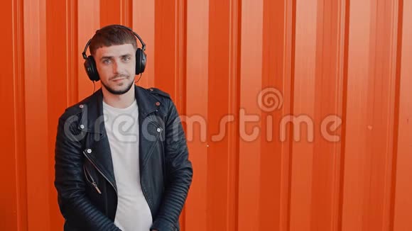 近橙色背景的年轻时尚积极男士耳机或耳机的肖像视频的预览图