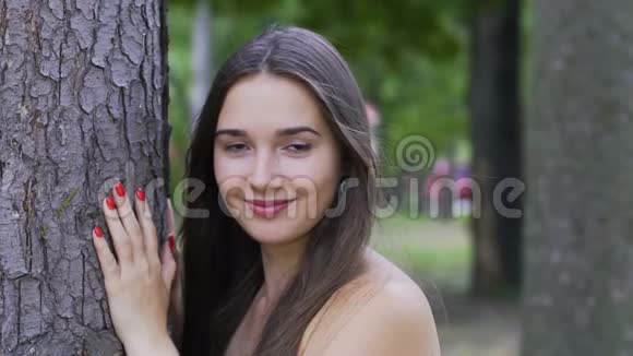 微笑的女人靠近树调情开放的外观美丽的微笑的女人户外视频的预览图