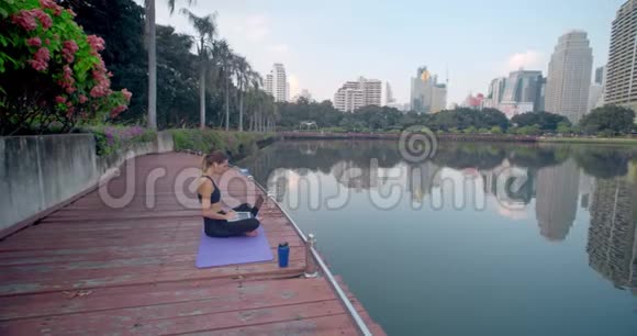 布鲁内特女士在湖边公园的午休时间使用笔记本电脑她坐在健身地毯上在上面打字视频的预览图