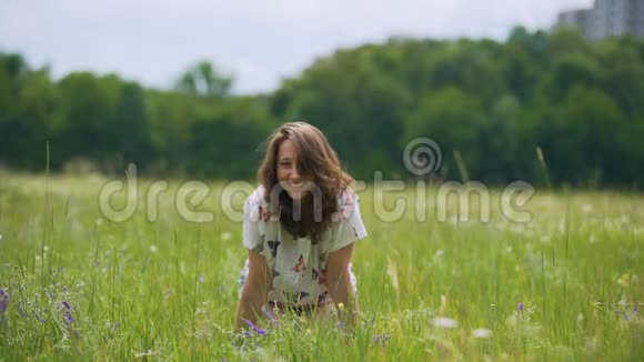 在绿草地上笑着年轻的黑发女人双手跪着视频的预览图