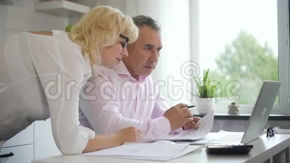 成熟的女性和男性养老金领取者在家里讨论投资视频的预览图