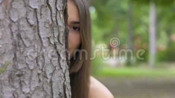 女人看在树后美丽的黑发冷静严肃的样子微笑慢动作视频的预览图