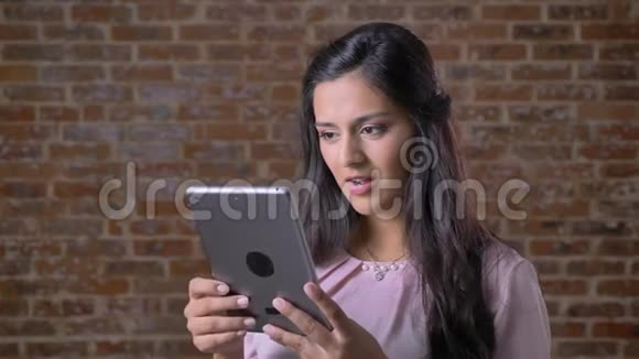 可爱的白种人女孩棕色的眼睛和长长的黑发高兴地展示着绿色屏幕的平板电脑而视频的预览图