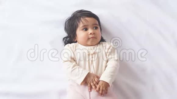 小可爱的小女孩举起身体躺在白色毯子上视频的预览图