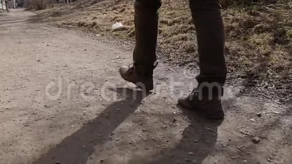 一个人走在城市的土路上他穿棕色裤子和靴子腿部的特写动作视频的预览图