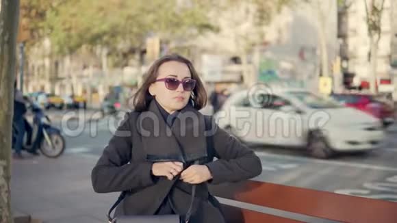女孩穿上外套坐在长凳上沿着街走视频的预览图