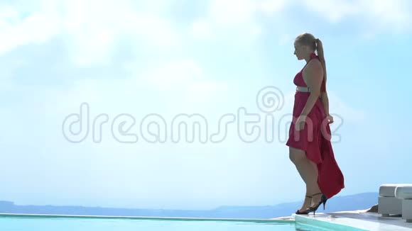 年轻女子沿着泳池边散步欣赏桑托里尼的壮丽景色视频的预览图