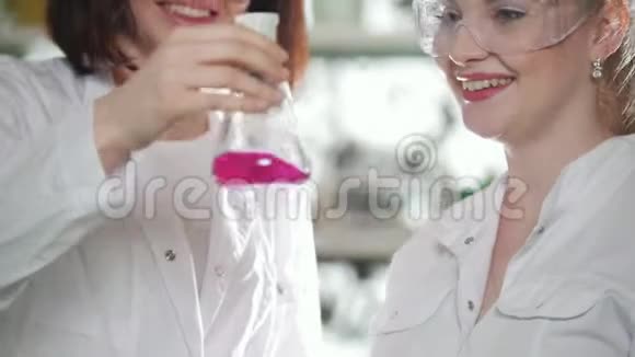 化学实验室两个年轻的实验室技术人员拿着一个装有粉红色液体的瓶子轻轻地摇动它视频的预览图