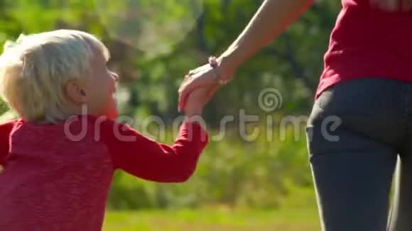 一个年轻女子和她的小儿子手牵着手从草坪上跑出来的慢镜头视频的预览图
