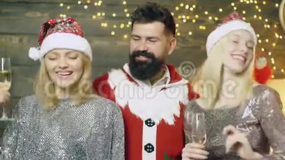 特写一个留胡子的男人和两个女孩庆祝新年和圣诞节穿着桑塔斯服装的男人和两个金发女郎视频的预览图