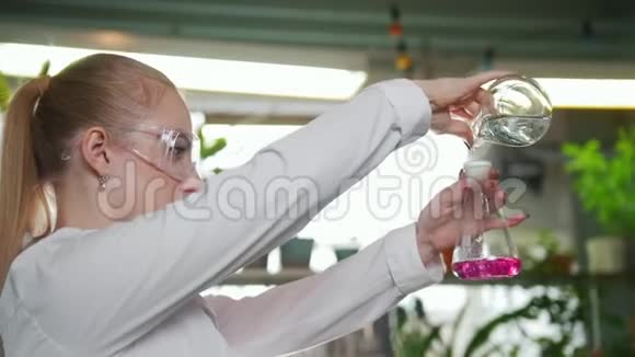 化学实验室年轻的金发女人把液体从一个瓶子倒到另一个瓶子视频的预览图