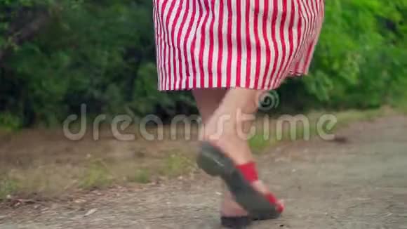 女腿在公园的人行道上行走一个穿凉鞋和条纹连衣裙的女孩走路女性腿的特写视频的预览图