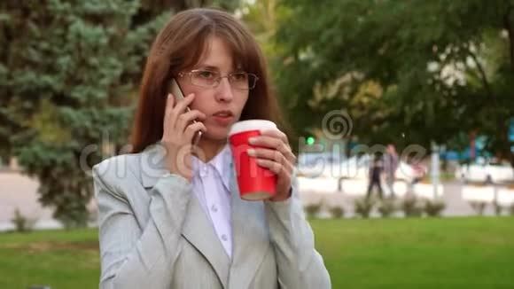 带眼镜的女商人在公园喝热咖啡在智能手机上聊天视频的预览图