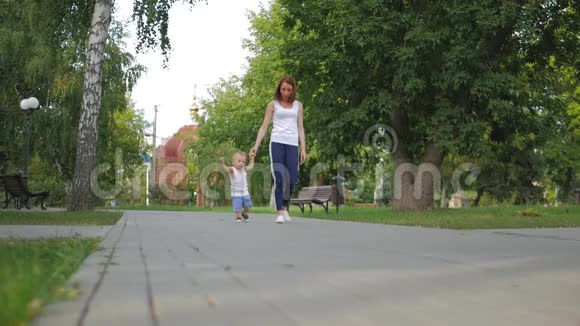 妈妈和儿子在公园里散步小男孩在夏天公园的第一步小男孩和妈妈在公园散步视频的预览图
