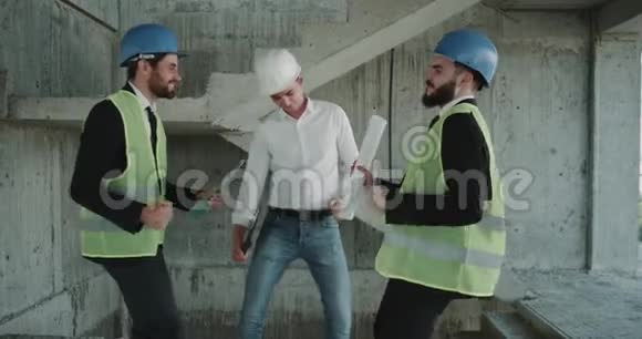三名建筑师在工作日结束时在工地上跳舞身穿能见度很高的背心穿着坚硬的衣服视频的预览图