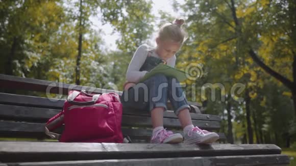 合上小美丽的学校女孩用彩色铅笔画画坐在阳光明媚的公园里的长凳上慢动作镜头视频的预览图