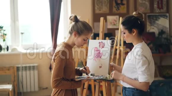 漂亮的女人绘画老师在美术课上教年轻女孩在调色板上混合颜料创造美丽的色彩视频的预览图