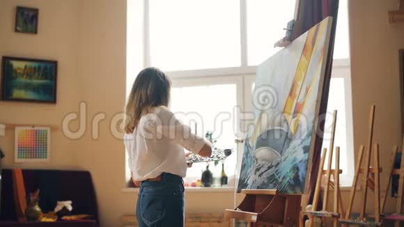 漂亮的女画家在调色板上混合颜料然后在画布上画海景创造出美丽的画面现代派视频的预览图