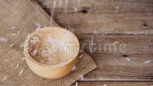 在木桌上用麻袋布将生的棕色全粒半精米倒入木碗的录像片段视频的预览图