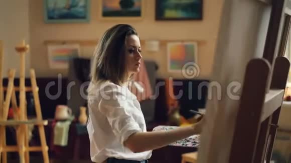 专业女艺术家正在画室用油画和画笔绘制海洋景观美丽的女孩视频的预览图