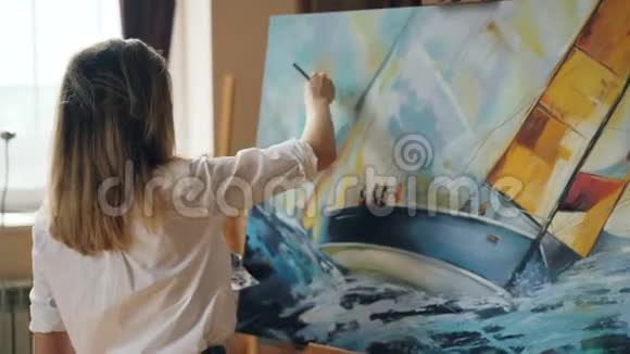 漂亮的女孩艺术家正忙于在画布上画海景使用调色板画笔和画架上的画布视频的预览图