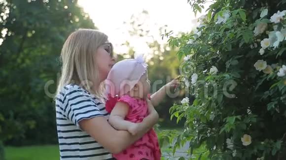 年轻的母亲抱着可爱的小女孩在公园里展示她的白色灌木花视频的预览图