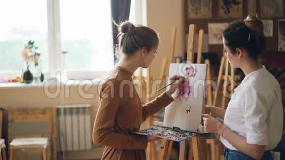 艺术学校的女学生正在用油画颜料画花而她的老师长得很漂亮的年轻女子正在给她送花视频的预览图
