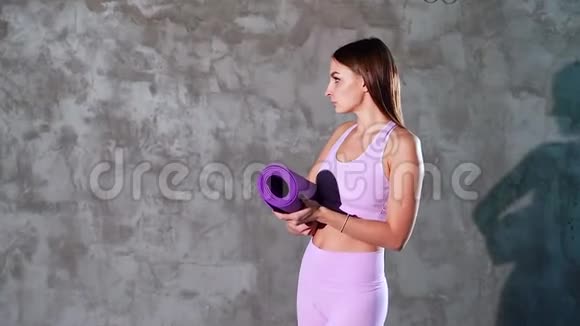 灰色背景上有瑜伽垫的年轻女人的肖像视频的预览图