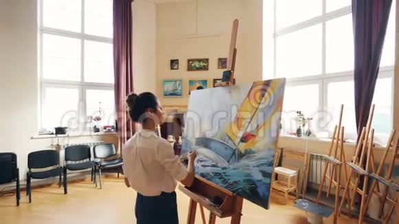 潘女士的镜头集中在画布上画海景在漂亮的灯光工作室里独自站在画架附近视频的预览图