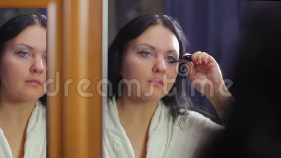 一个穿着白色外套的年轻女人在镜子前用睫毛膏画下睫毛视频的预览图