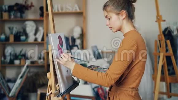 漂亮苗条的女孩正在用油画颜料画笔和调色板绘制花朵并在画布上作画视频的预览图