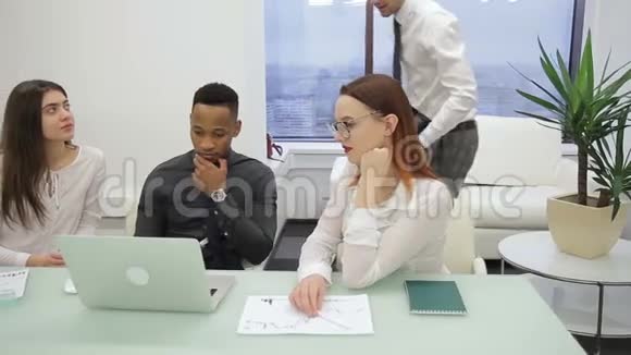 在办公室的办公桌上一个多族裔的团队一个领导看着笔记本电脑视频的预览图