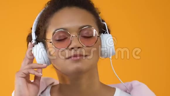 戴着白色耳机欣赏黄色背景音乐声音的漂亮年轻女子视频的预览图
