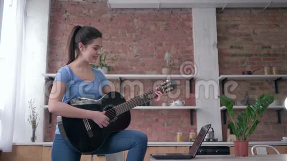 音乐教育快乐美丽的吉他手女孩学习演奏弦乐器使用笔记本电脑与视频的预览图