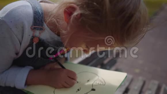 合上小美丽的学校女孩用彩色铅笔画画坐在阳光明媚的公园里的长凳上慢动作镜头视频的预览图
