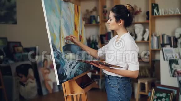 开朗的年轻女子艺术家是用油画画美丽的图画海洋风景然后看杰作视频的预览图