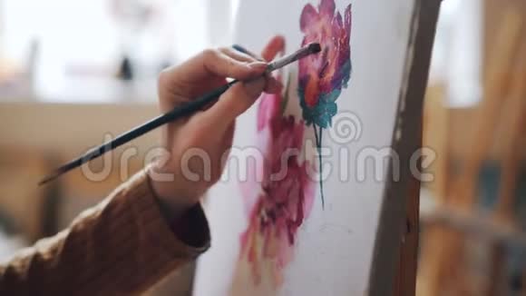 特写镜头女性手拿画笔在灯光工作室的画布上画鲜艳的花朵图案艺术视频的预览图