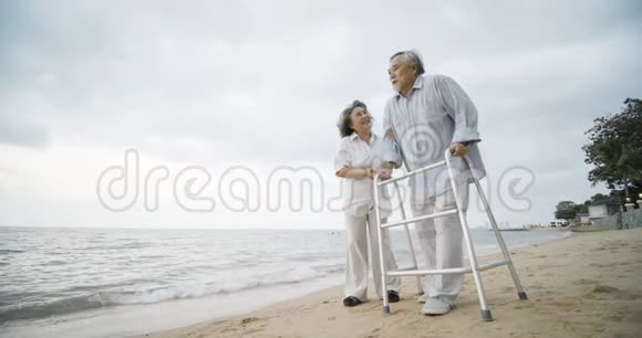 老人与沃克和他的妻子一起锻炼帮助他沿着海滩散步视频的预览图