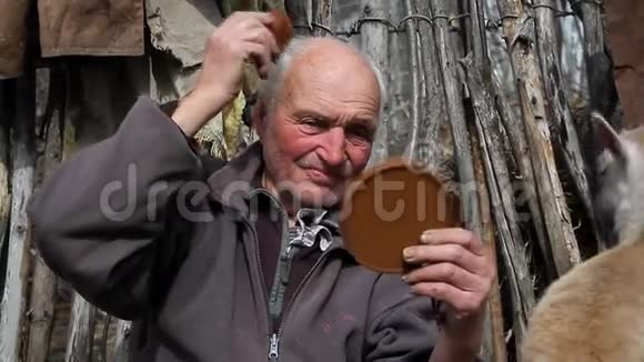老人坐在农场上的一个树桩上手里拿着一面镜子梳着头发站起来视频的预览图