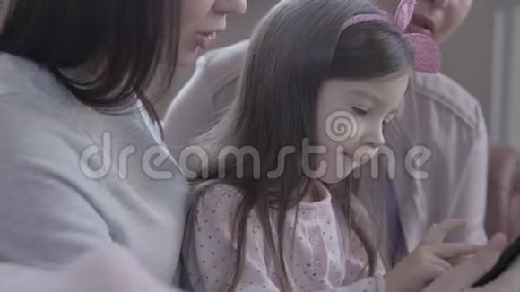 祖母母亲和小女儿一起坐在现代公寓的沙发上妈妈拿着小玩意的女孩视频的预览图