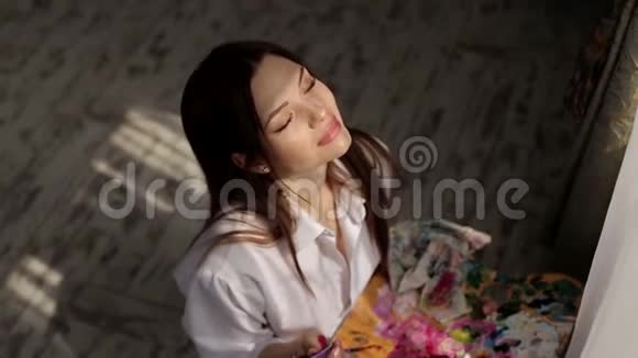 一个快乐的女孩艺术家在工作室的肖像他的手中有一个调色板的颜色视频的预览图