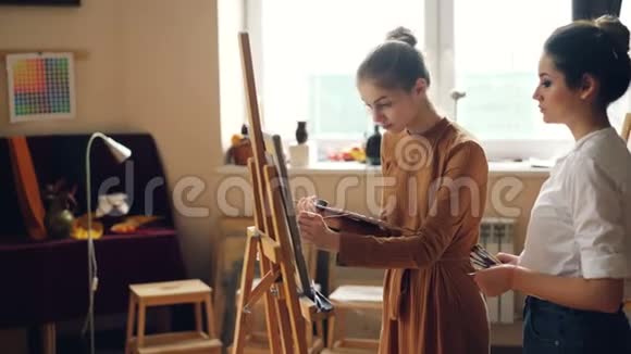 快乐的艺术学生在画布上用画笔绘画而她的老师正在检查她的作品和视频的预览图